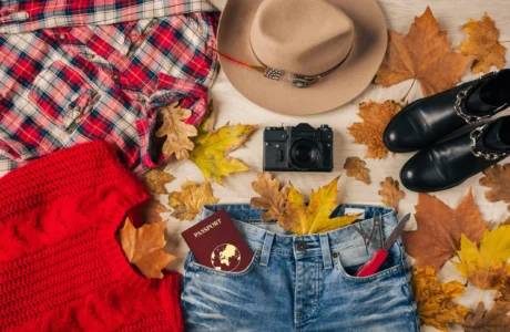 Flat lay of red sweater, plaid shirt, jeans, boots, hat, camera and passport for March most-loved products blog