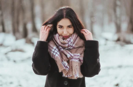 Woman wearing earmuffs and scarf outdoors in snowy winter weather for skin hydration blog