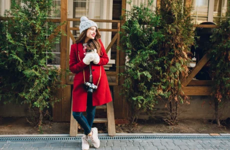 Woman in red winter coat with knit hat and gloves holding coffee and camera for winter weekend getaway blog