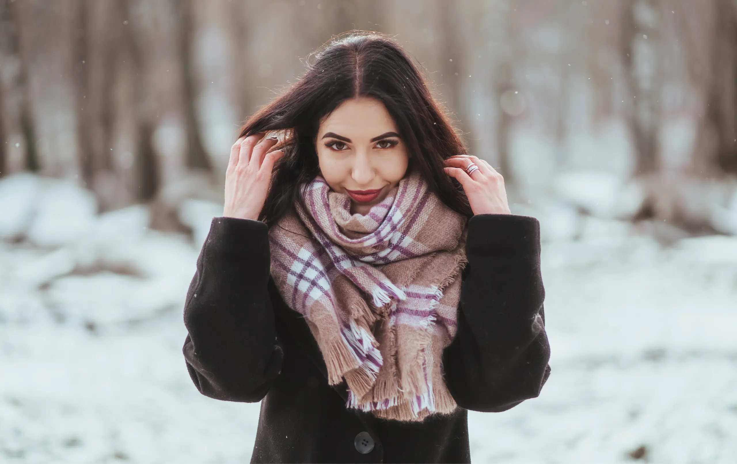 Woman wearing earmuffs and scarf outdoors in snowy winter weather for skin hydration blog
