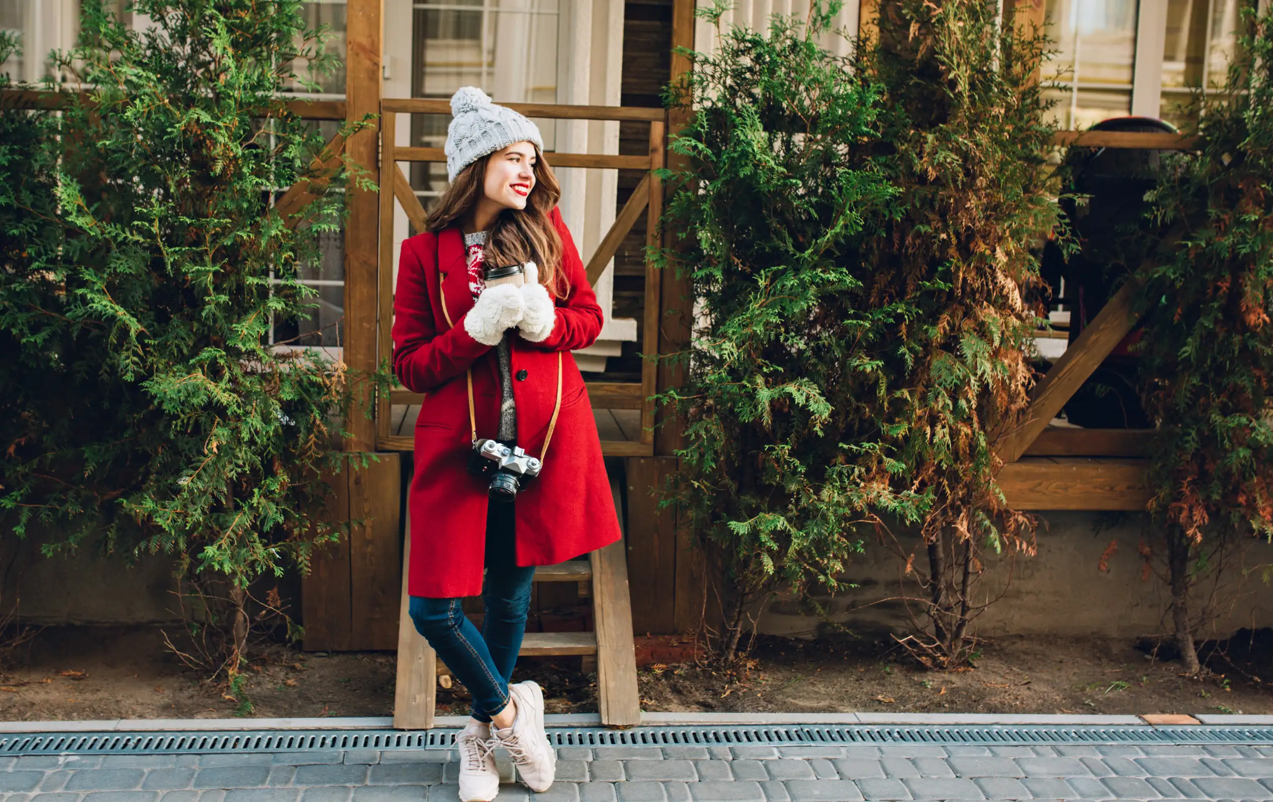 Woman in red winter coat with knit hat and gloves holding coffee and camera for winter weekend getaway blog